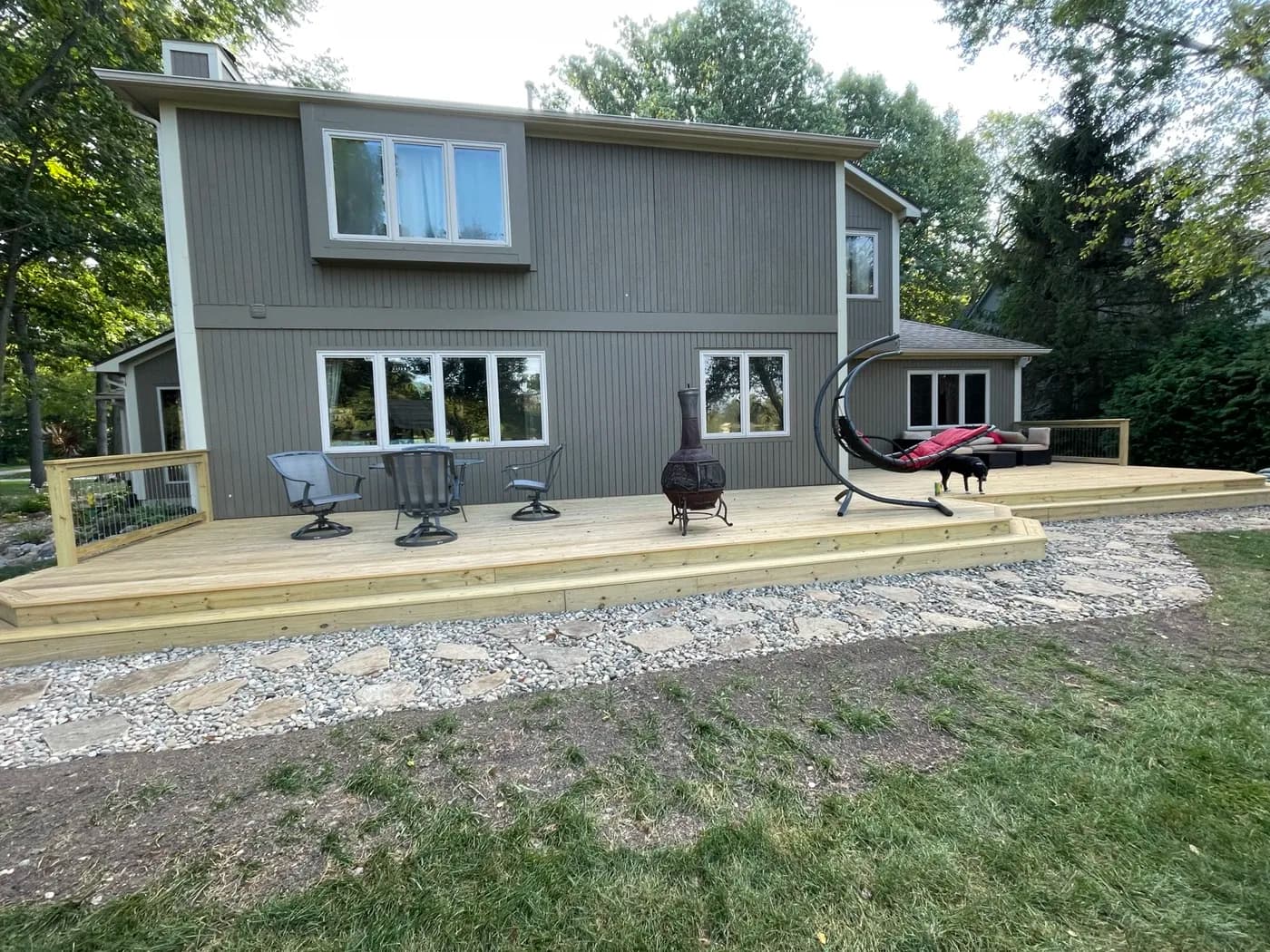 Wide view of a backyard deck with stone walkway and fire pit area